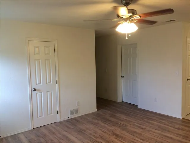 an empty room with wooden floor fan and windows