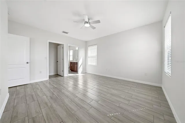 a view of an empty room with wooden floor and a ceiling fan