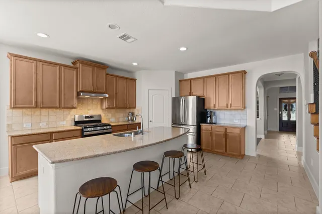 a kitchen with stainless steel appliances a stove a sink a refrigerator white cabinets a dining table and chairs