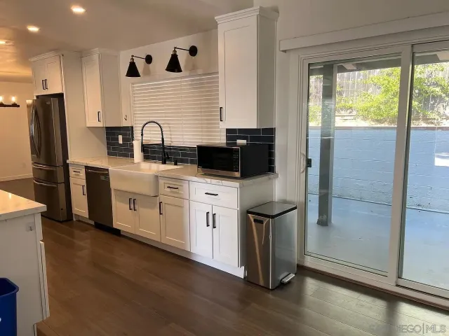 a kitchen with stainless steel appliances granite countertop a refrigerator a sink a stove and white cabinets with wooden floor