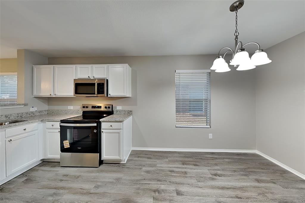 8844 Quarry Ridge Trail Fort Worth, TX 76244 - Photo 4 of 18 Kitchen featuring appliances with stainless steel finishes, white cabinetry, light wood finished floors, hanging light fixtures, and light stone countertops