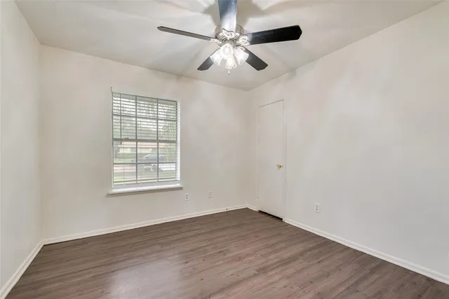 an empty room with wooden floor ceiling fan and windows