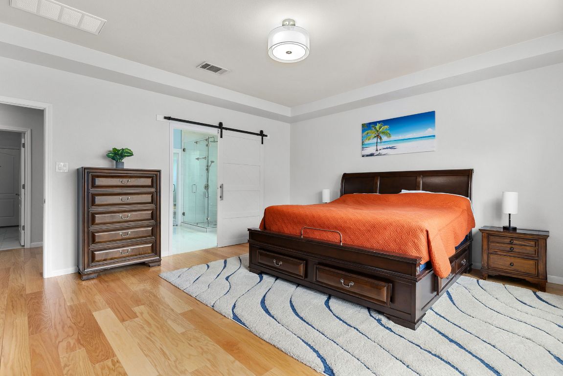 701 Old Ravine Court Round Rock, TX 78665 - Photo 15 of 40 Bedroom with a barn door, light wood finished floors, and connected bathroom