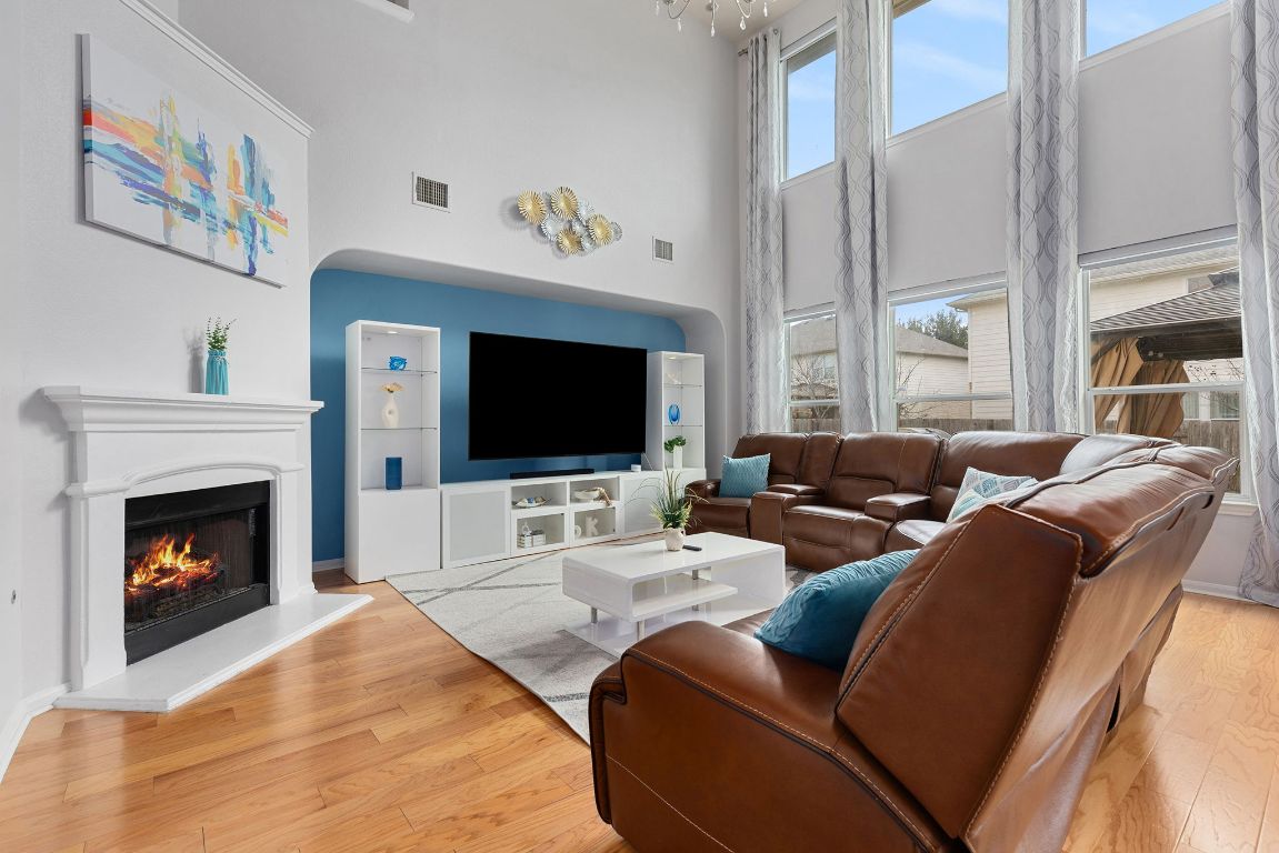 701 Old Ravine Court Round Rock, TX 78665 - Photo 2 of 40 Living room with a towering ceiling, a lit fireplace, and light wood-style floors