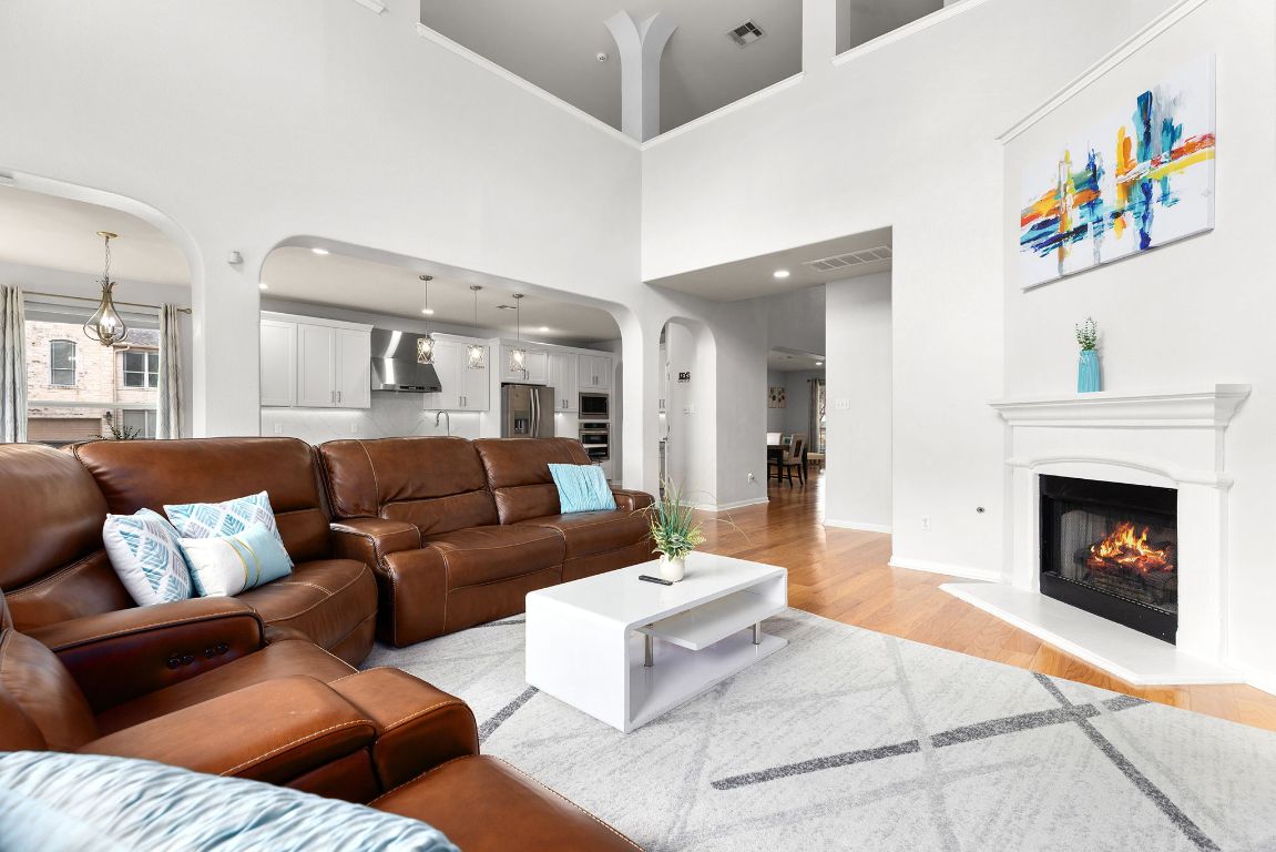 701 Old Ravine Court Round Rock, TX 78665 - Photo 5 of 40 Living area featuring arched walkways, light wood-type flooring, a glass covered fireplace, and a towering ceiling