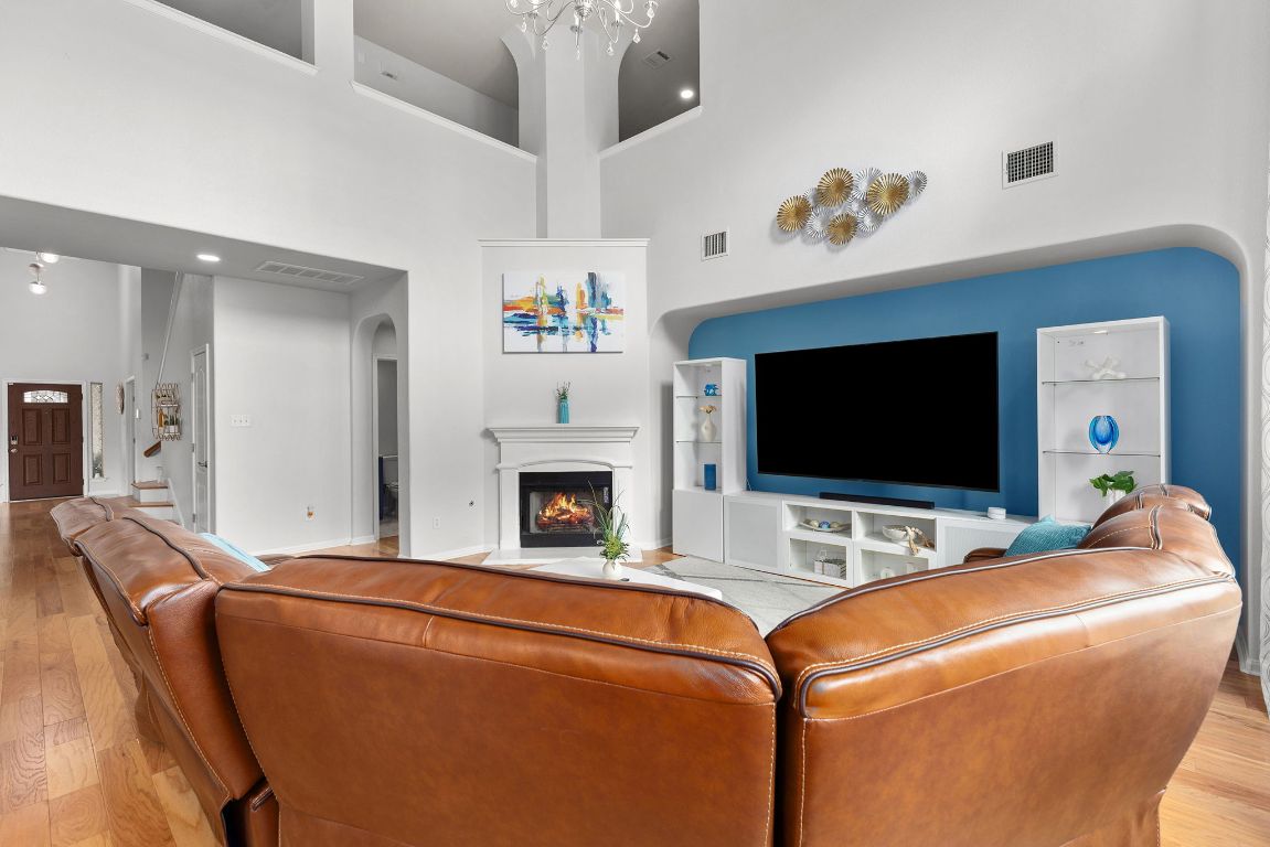 701 Old Ravine Court Round Rock, TX 78665 - Photo 6 of 40 Living area with light wood-style flooring, a lit fireplace, arched walkways, and a towering ceiling