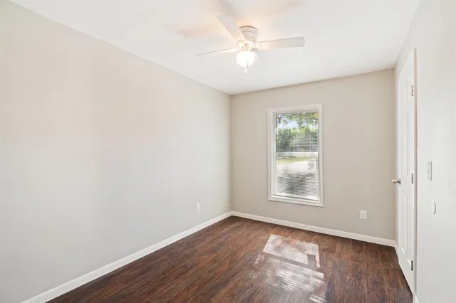 an empty room with wooden floor chandelier fan and windows