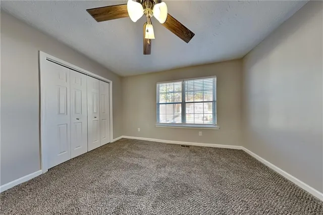 an empty room with chandelier fan and windows