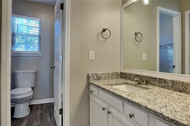 a bathroom with a granite countertop sink a toilet and a window