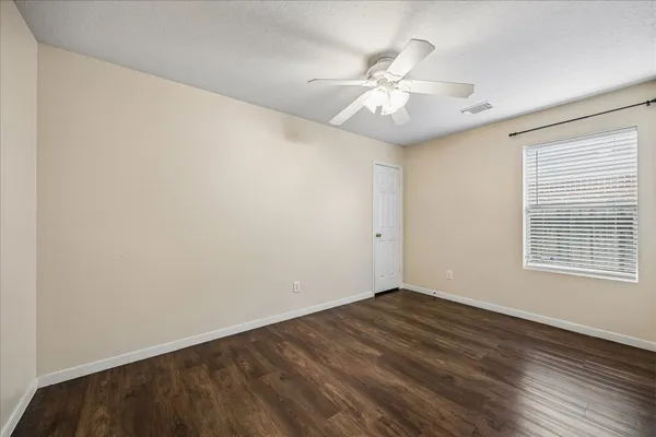 an empty room with wooden floor fan and windows