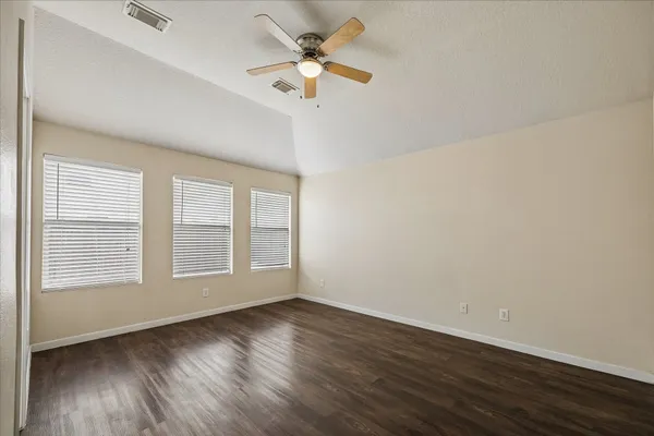 an empty room with wooden floor fan and windows