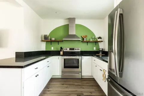 a kitchen with granite countertop a stove a sink and white cabinets with wooden floor