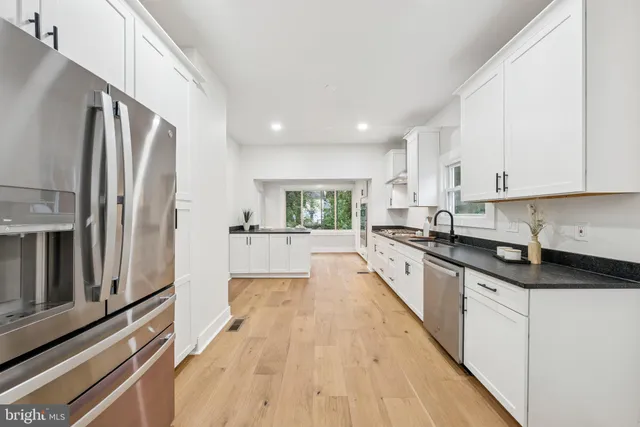 a large kitchen with stainless steel appliances granite countertop a refrigerator a sink dishwasher a stove and white countertops with wooden floor