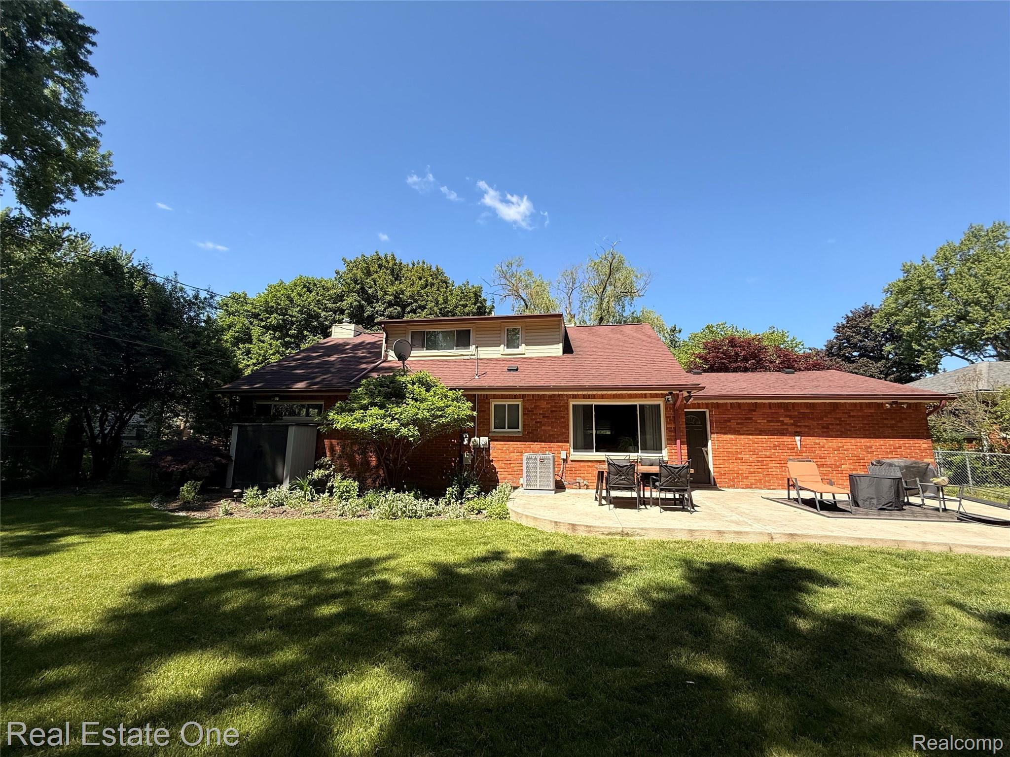 2189 Devonshire Road Bloomfield Hills, MI 48302 - Photo 40 of 50 Expansive rear yard featuring a brick facade structure with a contrasting roof, a large wooden deck, and mature perimeter trees