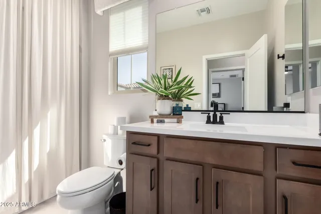 a bathroom with a toilet a sink a mirror a window and vanity