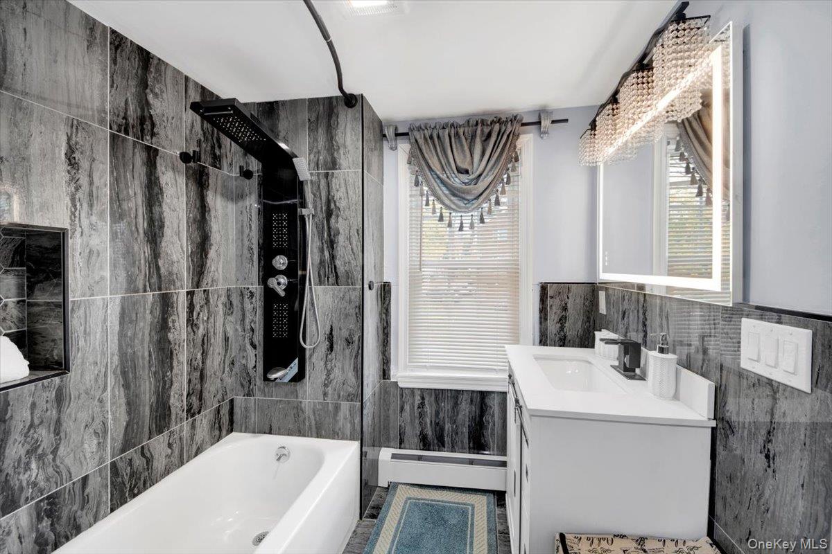 75 West Kingsbridge Road Mount Vernon, NY 10550 - Photo 24 of 37 Full bath featuring tile walls, washtub / shower combination, vanity, a baseboard heating unit, and plenty of natural light
