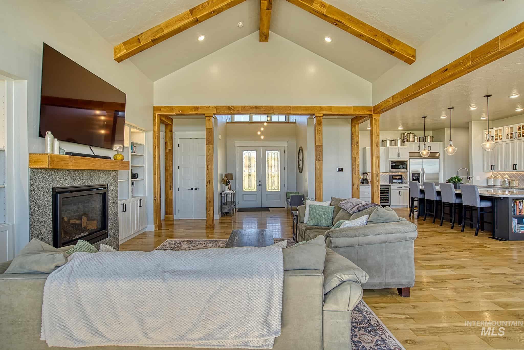 876 Coyote Gulch Road Adrian, OR 97901 - Photo 27 of 50 Vaulted ceilings with exposed wood beams, a fireplace with a stone surround and wood mantel, built-in shelving, wood-finish flooring, and a kitchen with pendant lighting