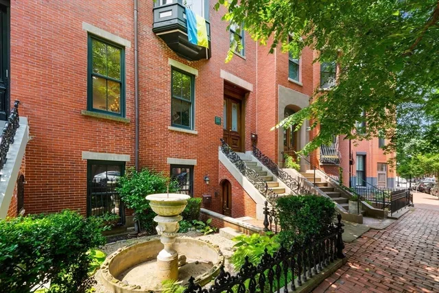a view of a house with brick walls plants and large tree