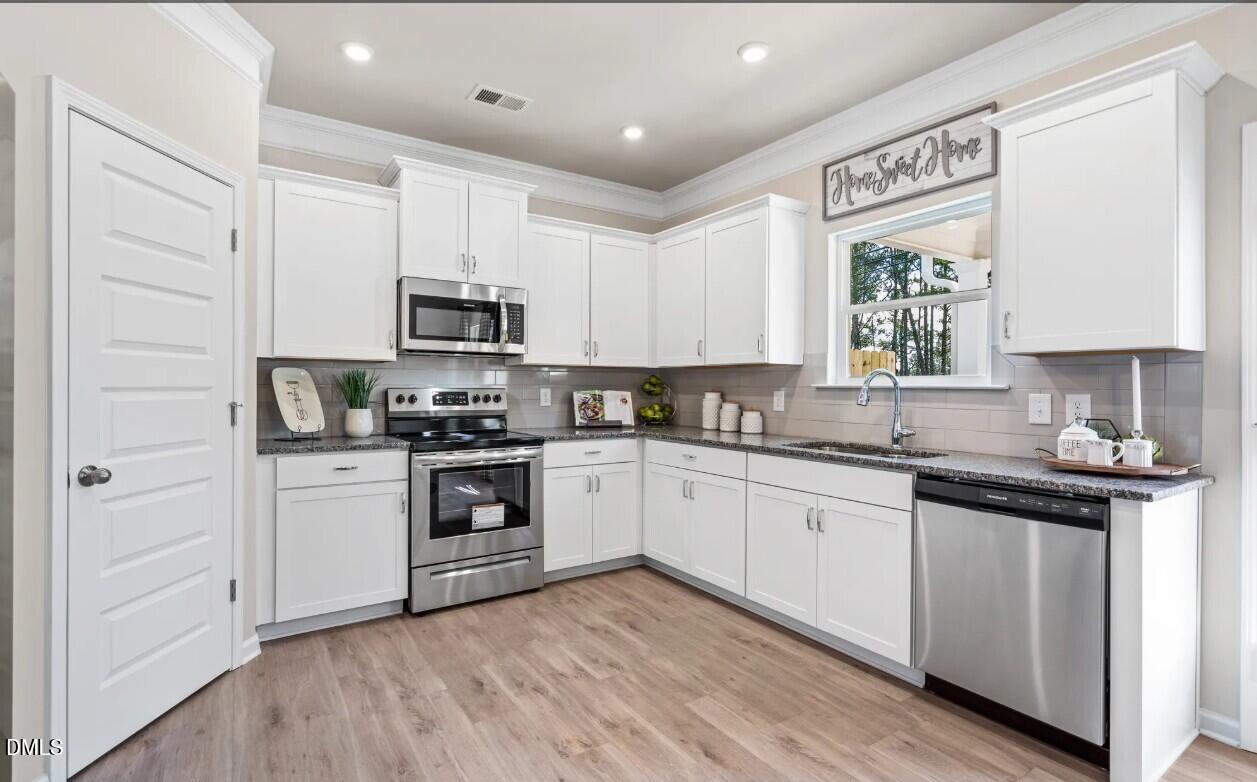 74 Floating Brg Trail Lillington, NC 27546 - Photo 3 of 7 a kitchen with granite countertop white cabinets and black stainless steel appliances