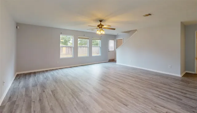 an empty room with wooden floor chandelier fan and windows