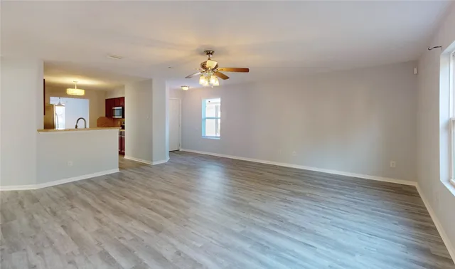 an empty room with wooden floor chandelier fan and windows
