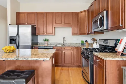 a kitchen with stainless steel appliances granite countertop a stove a sink dishwasher and a refrigerator with wooden cabinets