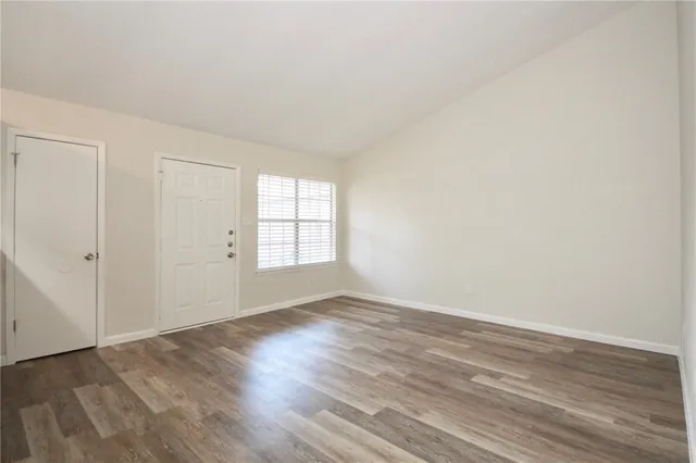 a view of an empty room with wooden floor and a window