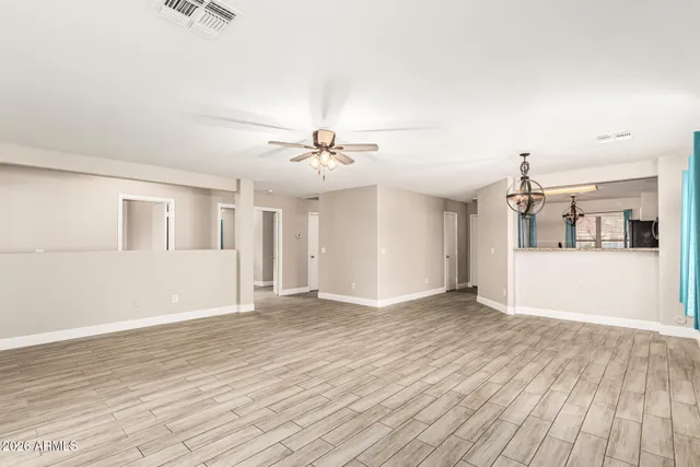 an empty room with wooden floor chandelier fan and windows