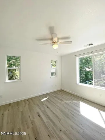 an empty room with wooden floor fan and windows
