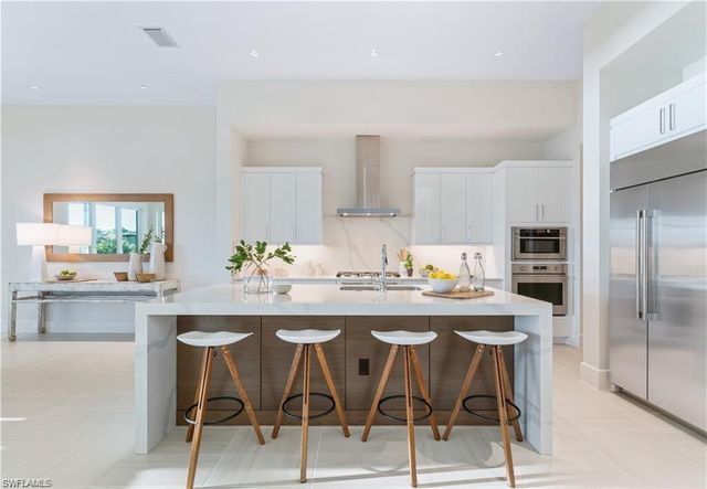 a kitchen with stainless steel appliances kitchen island granite countertop a dining table chairs and a refrigerator