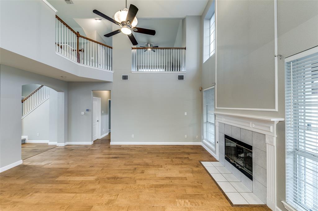 4532 Crown Ridge Drive Plano, TX 75024 - Photo 4 of 25 Spacious living area featuring high ceilings, wood-finish flooring, a tile fireplace, multiple windows with blinds, and a second-story balcony overlooking the room