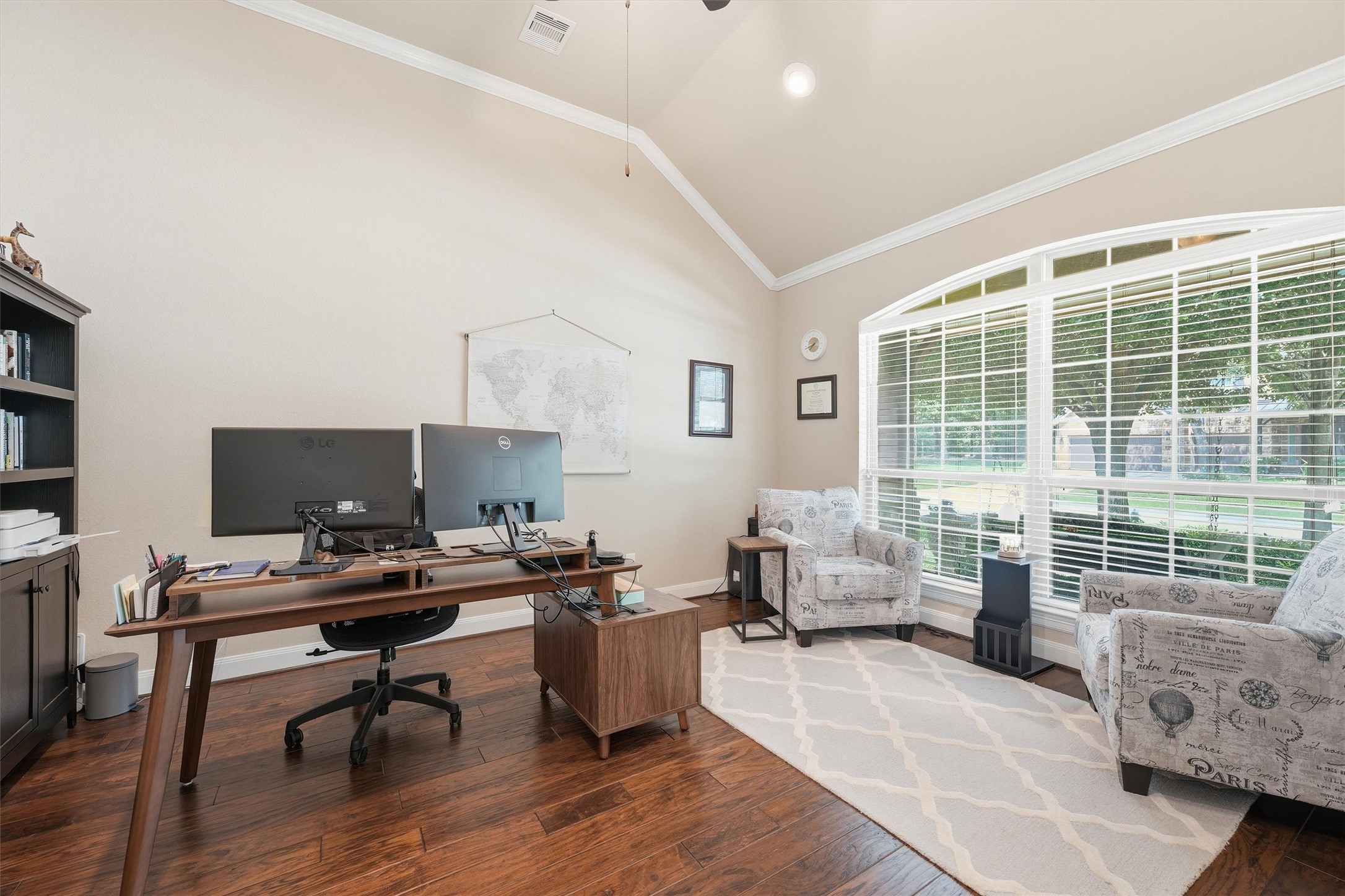 17710 Rough River Court Humble, TX 77346 - Photo 5 of 38 Bright home office with high ceilings, featuring a large arched window, wood flooring, and a spacious desk setup. Cozy seating area with two upholstered chairs and a patterned rug. Ideal for productivity and relaxation.