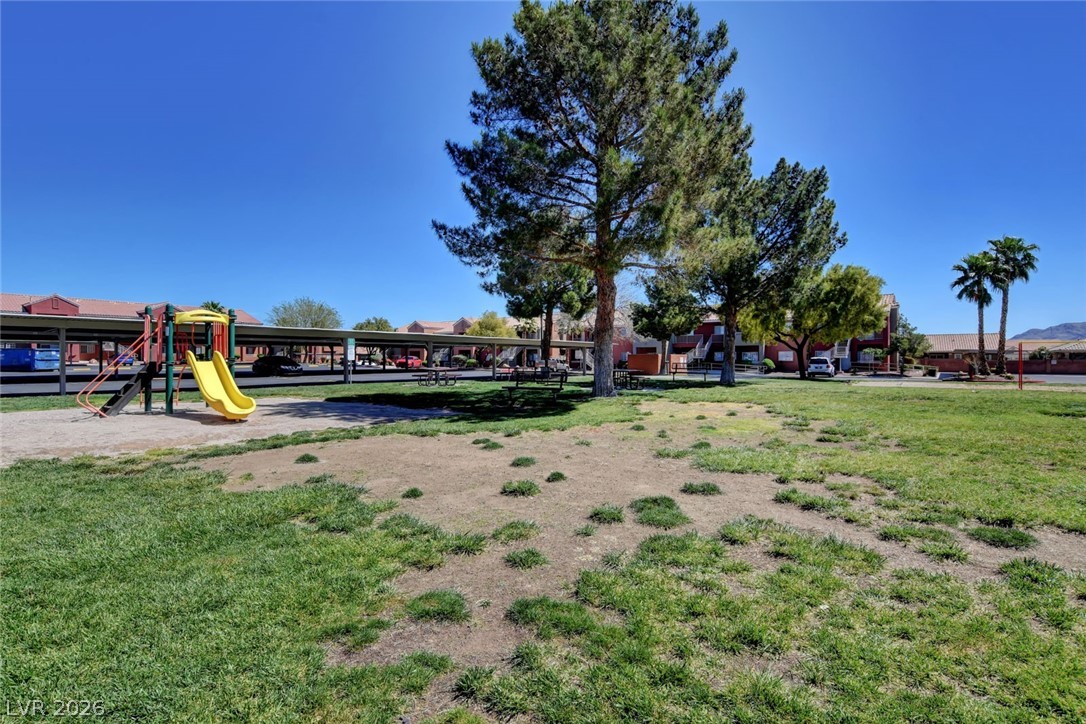 4730 East Craig Road, Unit 1155 Las Vegas, NV 89115 - Photo 27 of 41 A community green space features a vibrant playground and shade trees, with residential buildings and covered parking beyond.