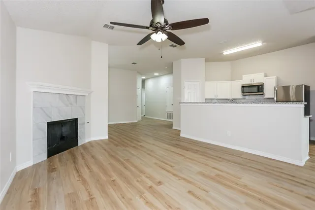 a large white kitchen with kitchen island a stove a refrigerator a sink and a fireplace with wooden floor