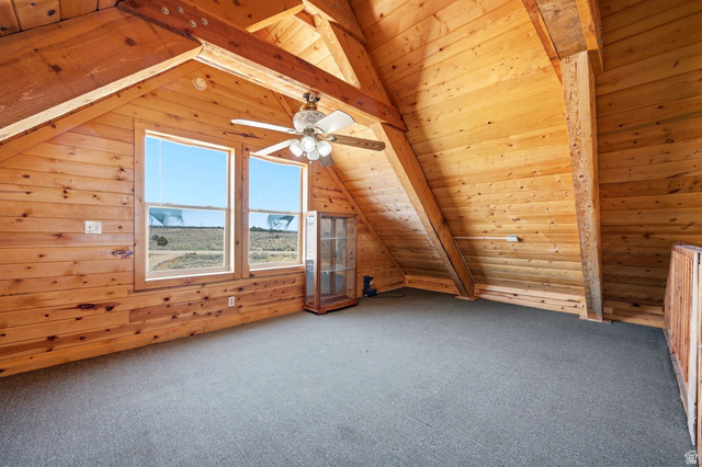 10937 South County Road, Unit 29 Duchesne, UT 84021 - Photo 23 of 41 Natural wood-paneled walls and ceilings featuring exposed wood beams, two large windows, a ceiling fan with integrated lighting, and neutral carpeting