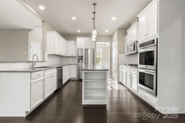 a kitchen with stainless steel appliances kitchen island granite countertop a stove a sink and white cabinets with wooden floor