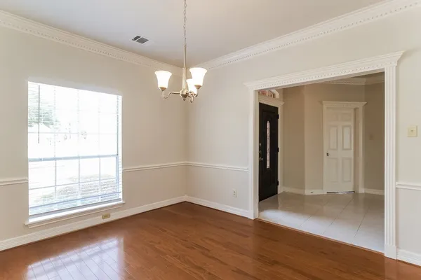 an empty room with wooden floor chandelier and windows