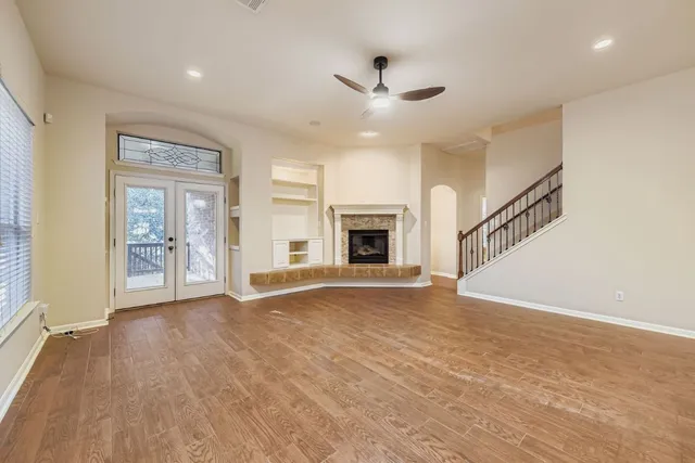 an empty room with wooden floor fireplace and windows