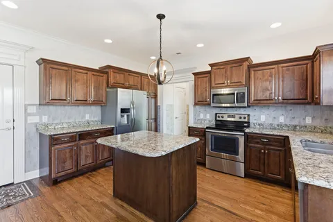 a kitchen with stainless steel appliances granite countertop a stove top oven a sink dishwasher and a refrigerator with wooden floor
