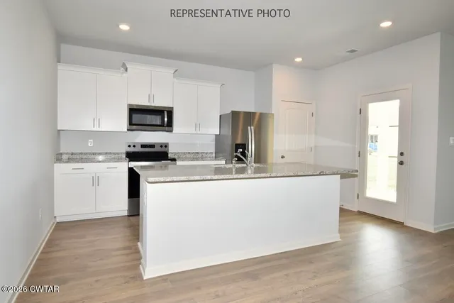 a view of kitchen with stainless steel appliances granite countertop a stove a sink a refrigerator and white cabinets with wooden floor