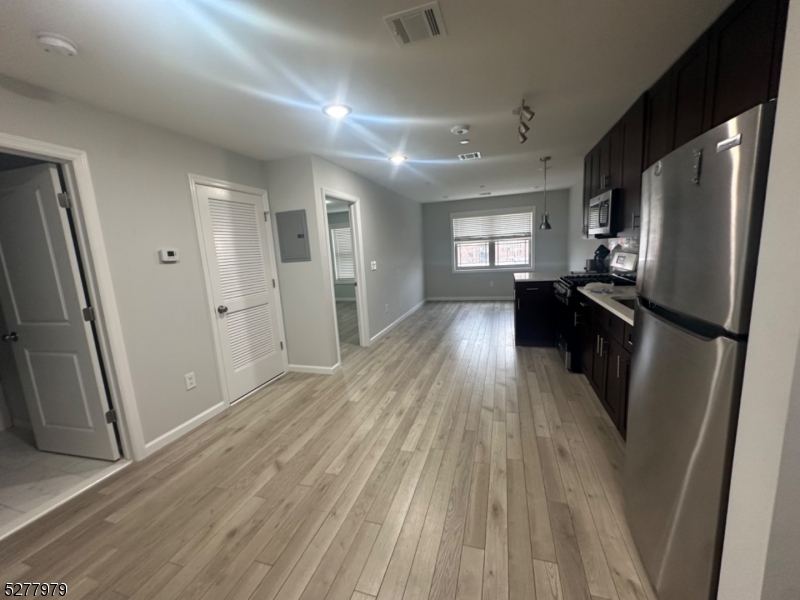 an empty room with wooden floor and a kitchen