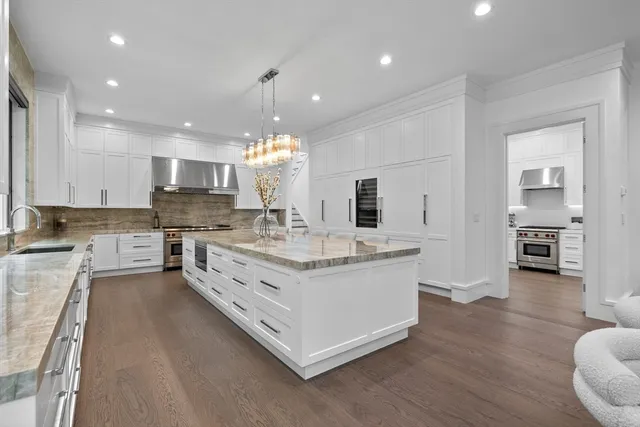 a large white kitchen with kitchen island a sink dishwasher a stove and white cabinets with wooden floor
