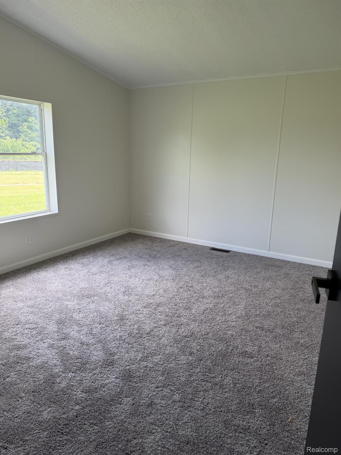 3586 Columbiaville Road Columbiaville, MI 48421 - Photo 7 of 10 Spacious room featuring gray carpeting, light-colored walls with vertical panel accents, and a window offering abundant natural light