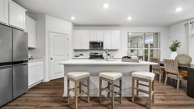 a kitchen with stainless steel appliances granite countertop a stove a sink a refrigerator a microwave a dining table and chairs with wooden floor