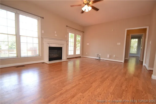 an empty room with wooden floor fireplace and windows