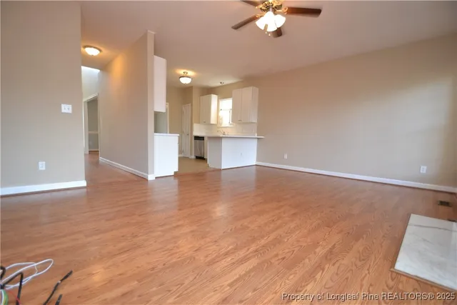 an empty room with wooden floor a ceiling fan and kitchen view