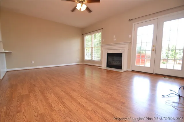 an empty room with wooden floor fireplace and windows