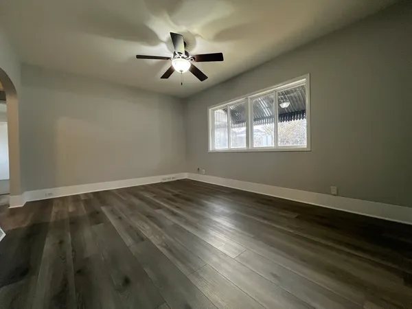 an empty room with wooden floor chandelier fan and windows