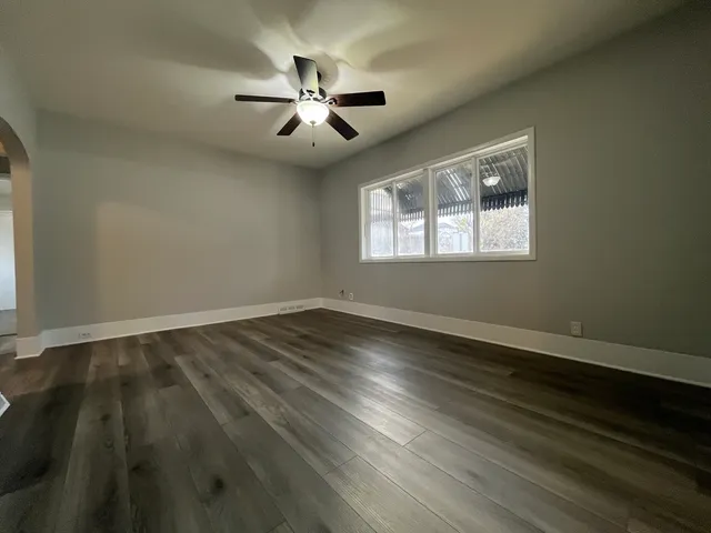 an empty room with wooden floor chandelier fan and windows