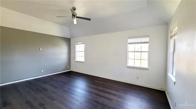 an empty room with wooden floor chandelier fan and windows